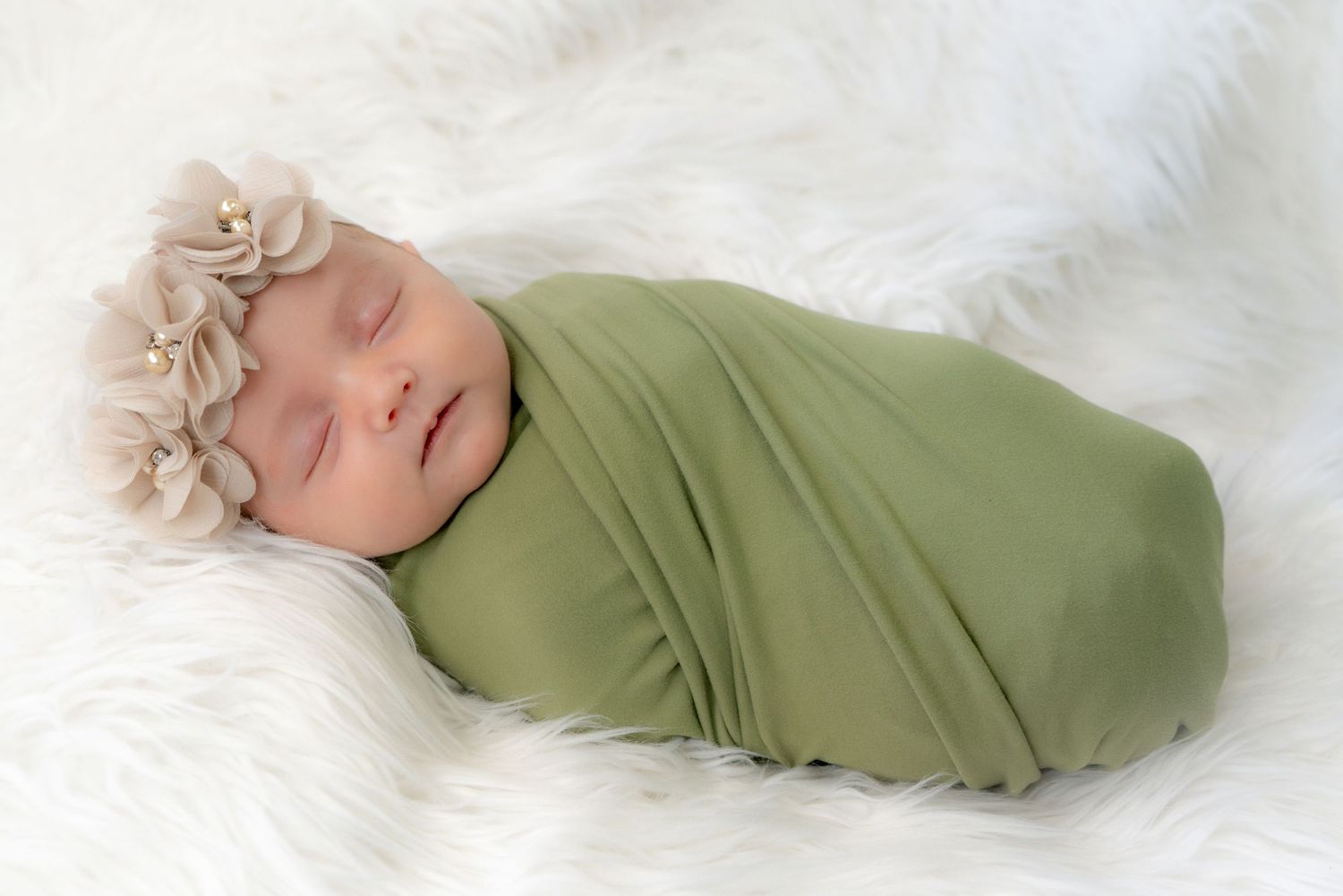 A sleeping baby swaddled in a purple floral blanket lies peacefully on soft white bedding.