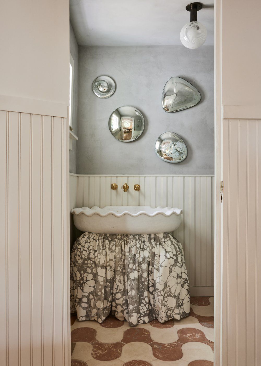 A tiled bathroom with paneled walls features floral curtains, curved brown floor tiles, and vintage wall-mounted fixtures.
