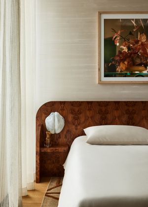 Modern bedroom interior with wooden headboard, white bedding, and framed floral artwork against light-colored walls.