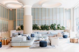 Modern hotel lobby interior with modular gray seating, blue ottoman poufs, and pastel wall panels with circular lighting.