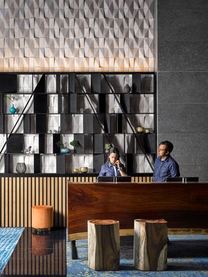 Modern office reception area with geometric wall panels, display shelving unit and wooden desk with log stools.