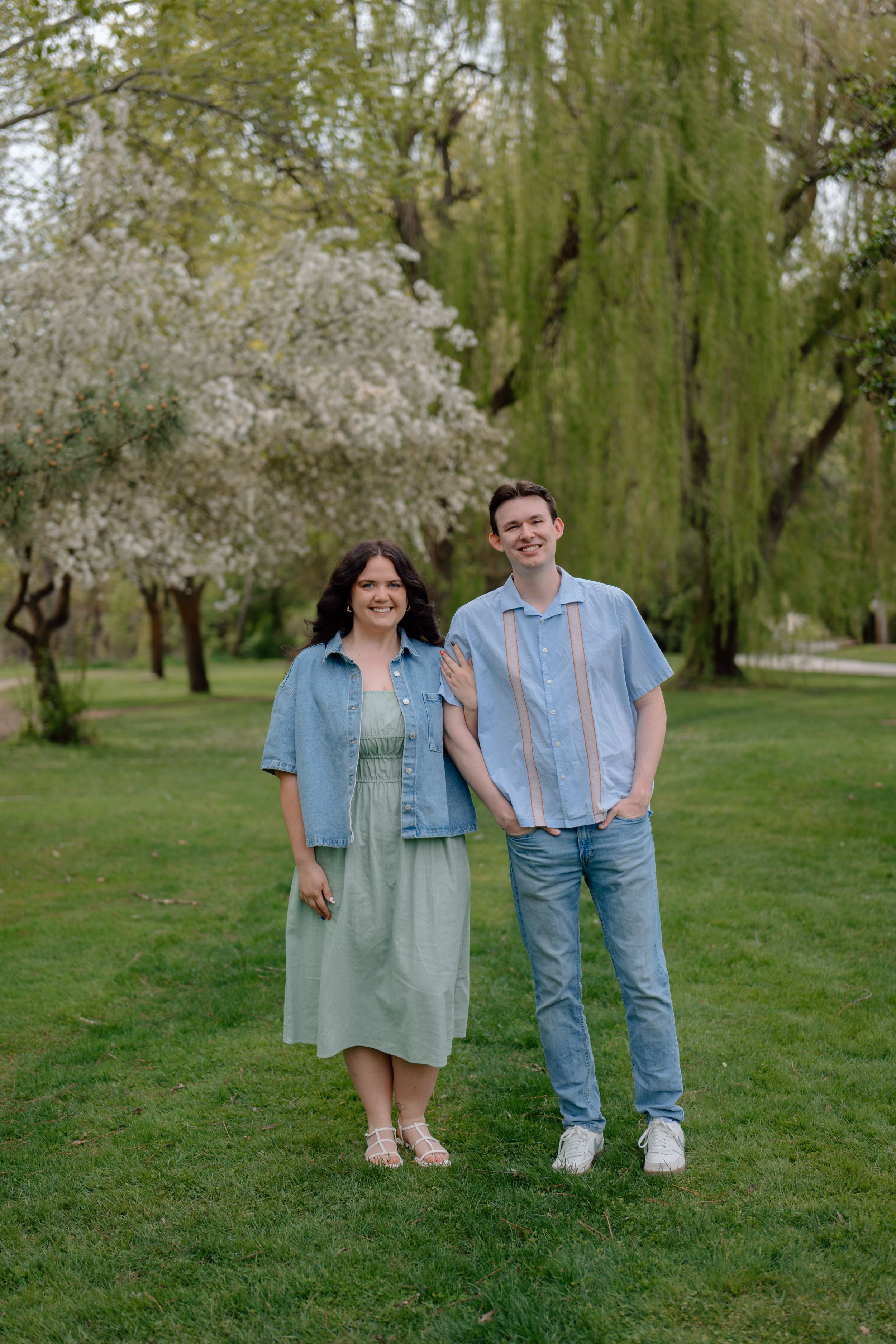 Spring photoshoot in a park with blooming trees and people wearing casual denim and green outfits.