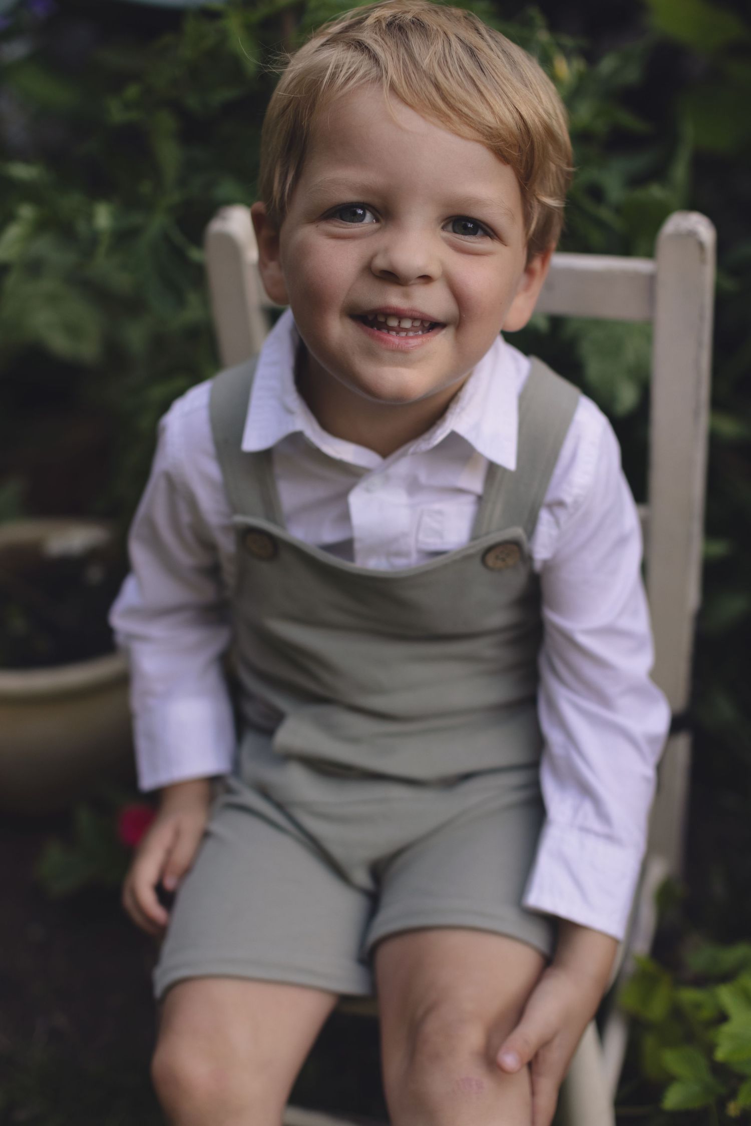 boy sits on a chair. garden mini session Candice and kids sit on a blanket under the trees that glow with summer sunshine