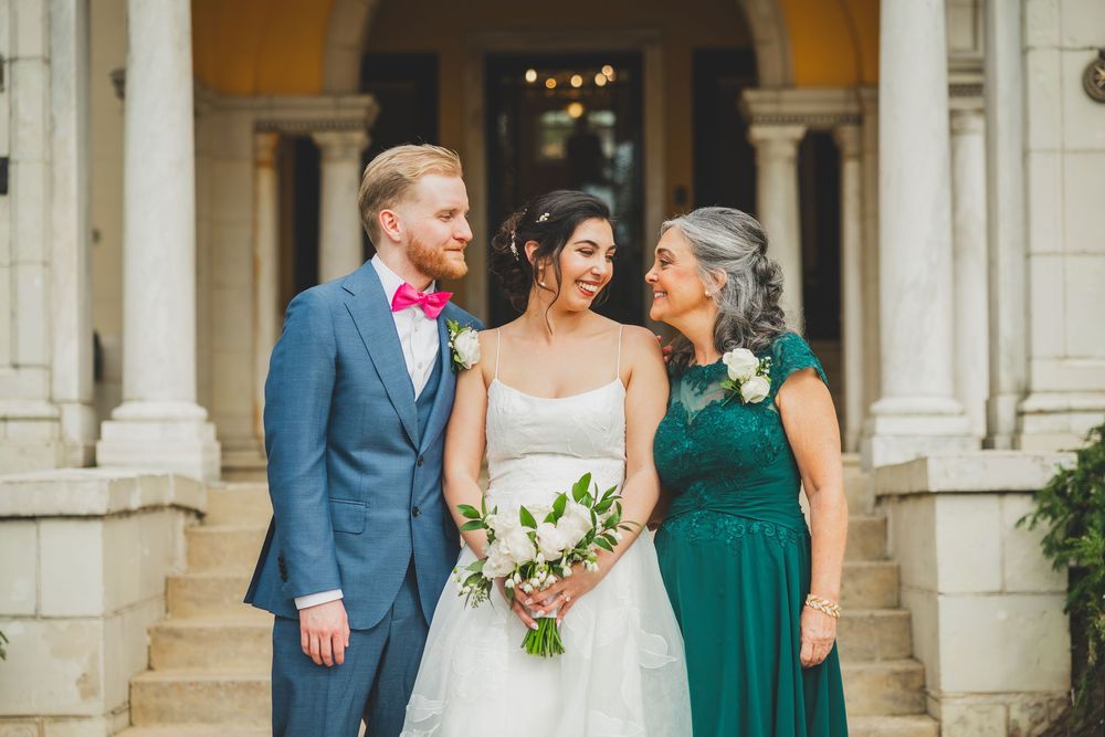 Wedding party members stand together in emerald green dresses and blue suits while holding white floral bouquets.