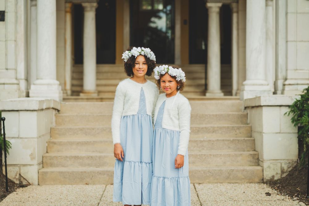 Flowergirls in matching light blue dresses lined up outdoors against a classic stone building facade at the Josephine Butler Parks Center