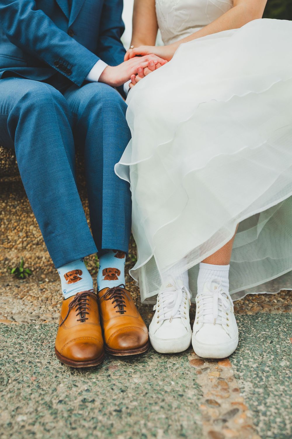 Newlywed couple showing fun sock fashion with brown leather shoes and white sneakers under wedding attire.