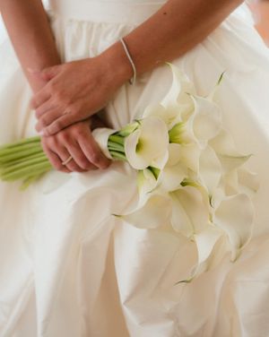 Beautiful white calla lily bouquet held against a flowing white wedding dress creating an elegant bridal detail.