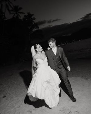 Joyful couple celebrating their wedding on a palm-lined beach at sunset in black and white photography.