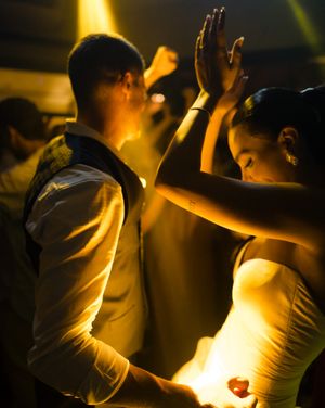 A couple dances intimately on the dance floor illuminated by warm yellow spotlights during a celebration.