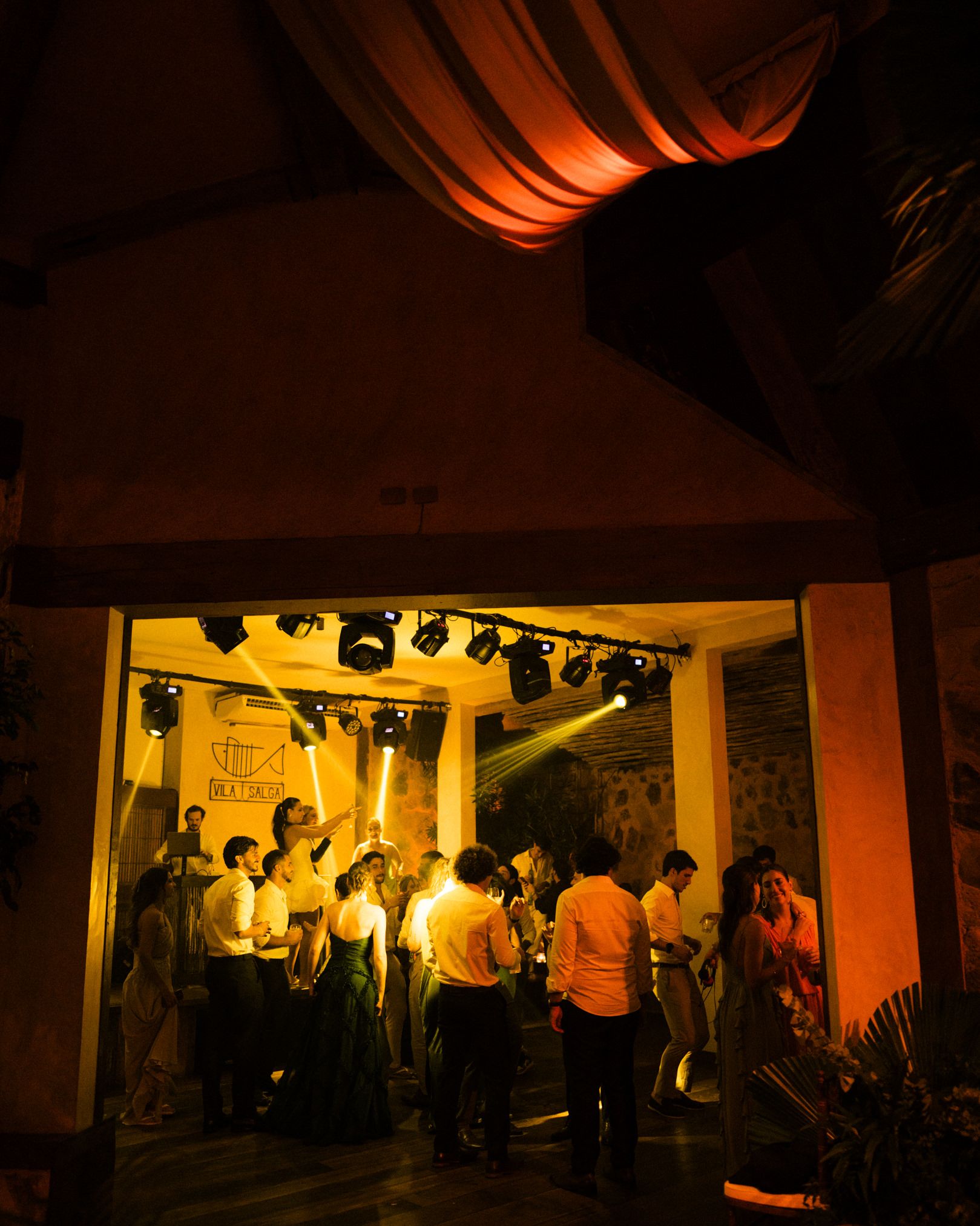 A dimly lit nightclub with orange lighting and people dancing and socializing in a crowded space.