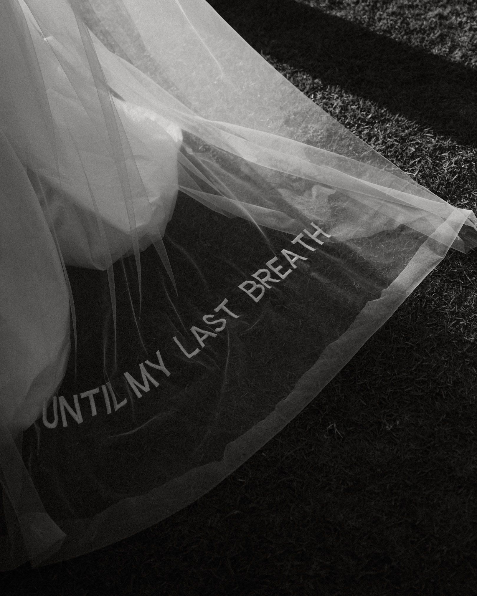 A delicate white veil with text reading 'UNTIL MY LAST BREATH' in black lettering against a dark background.