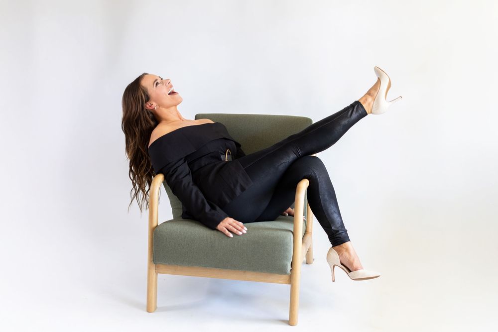 Person in black loungewear relaxing in multiple poses on a minimalist wooden chair against a white background.