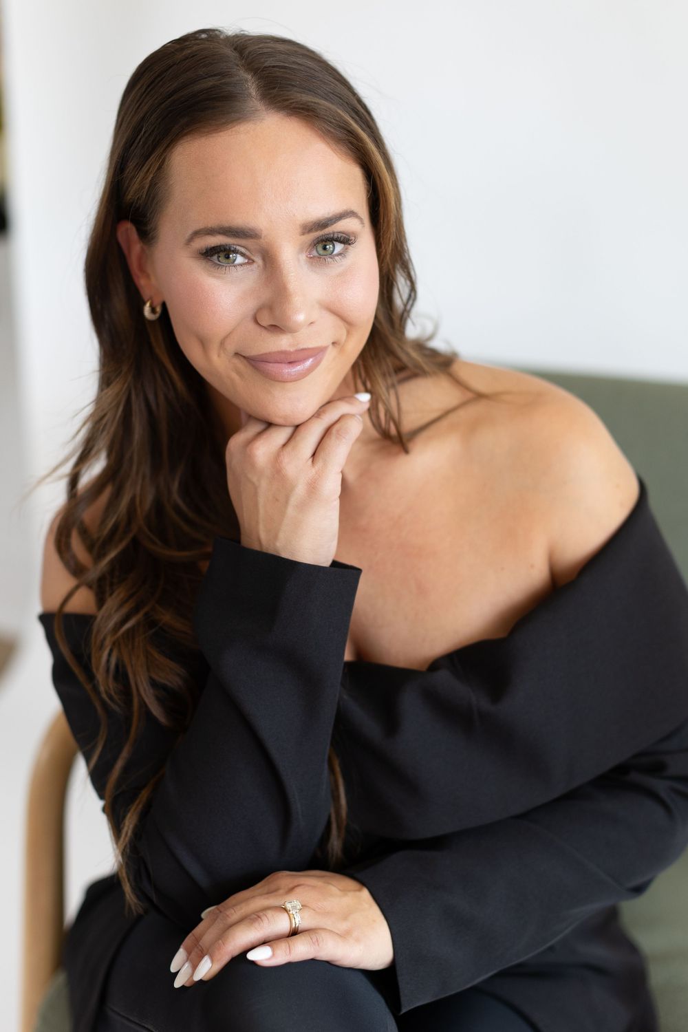 Portrait in a classic black off-shoulder top showing a warm smile and elegant pose with manicured nails.