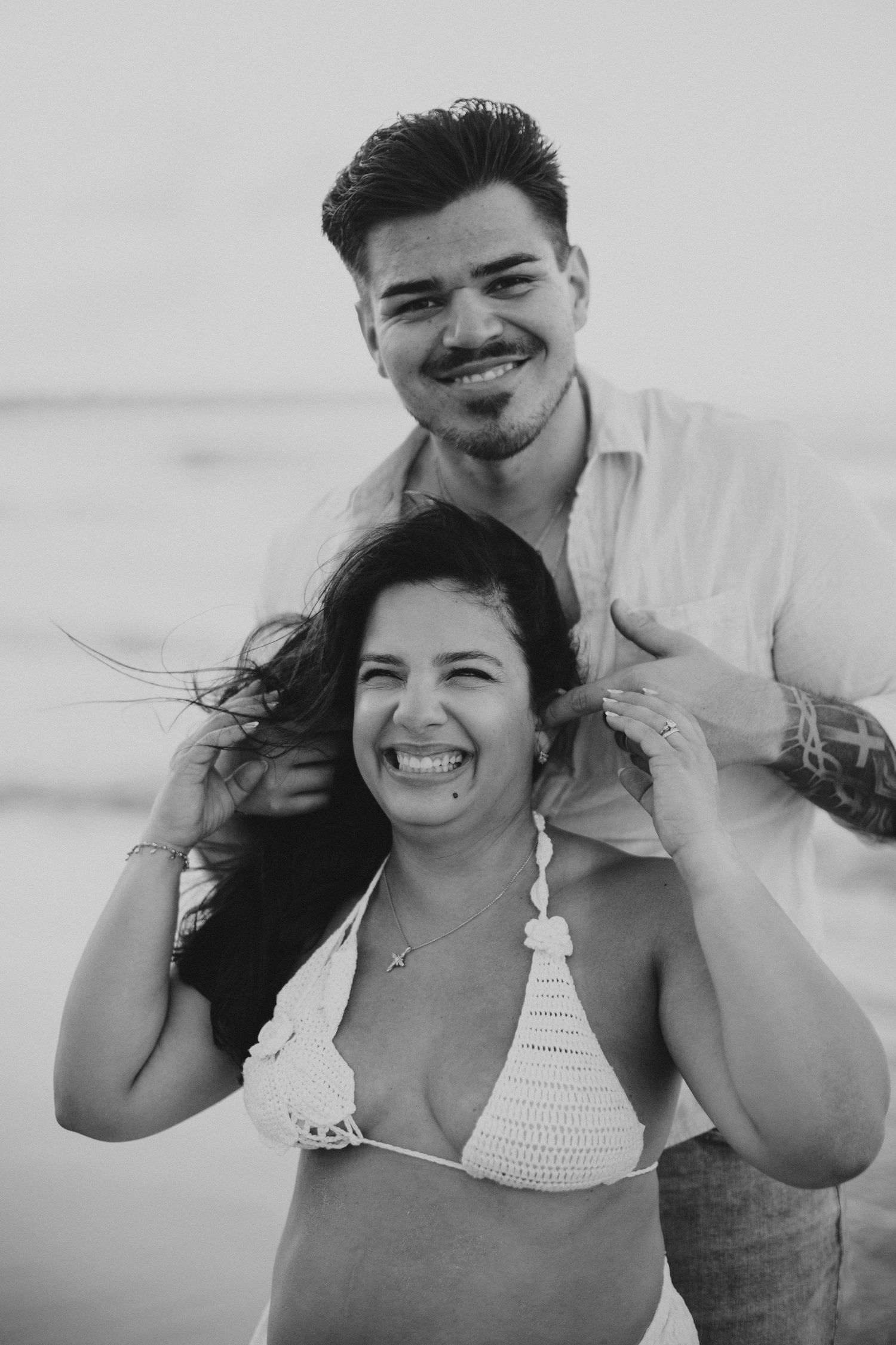A couple shares a joyful moment together on the beach in black and white.