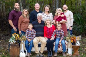 A group poses together outdoors in coordinated autumn outfits for a family photo session in a wooded setting.