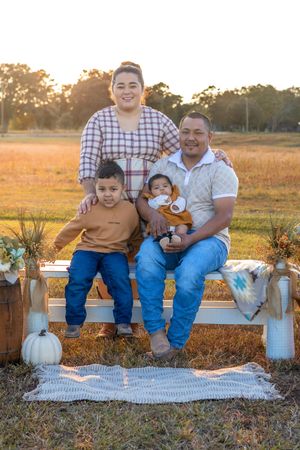Family sitting together on a blanket outdoors during golden hour with pumpkin and rustic fall decor.