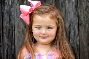 Toddler portrait with pink bow accessory with rustic wooden backdrop.