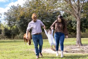 Family walking together through a sunny field with trees.