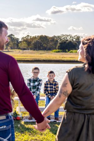 Two people stand by the water at sunset while others gather for an outdoor event by the shoreline.