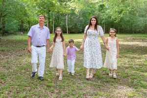 Family of five holding hands walking outdoors in a lush green wooded park, dressed in coordinating pastel outfits.
