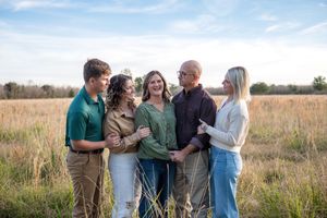 A group of people stand together in conversation against a scenic golden field at sunset.
