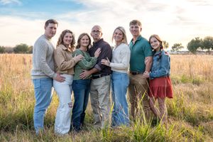 A group of people pose together in casual attire against a golden field at sunset.