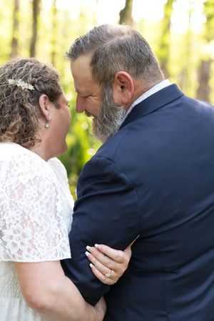 Bride and groom share an intimate moment outdoors, her lace dress and diamond ring visible as they lean foreheads together.