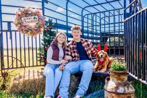 Couple posing for Christmas portrait on horse trailer with their dog.