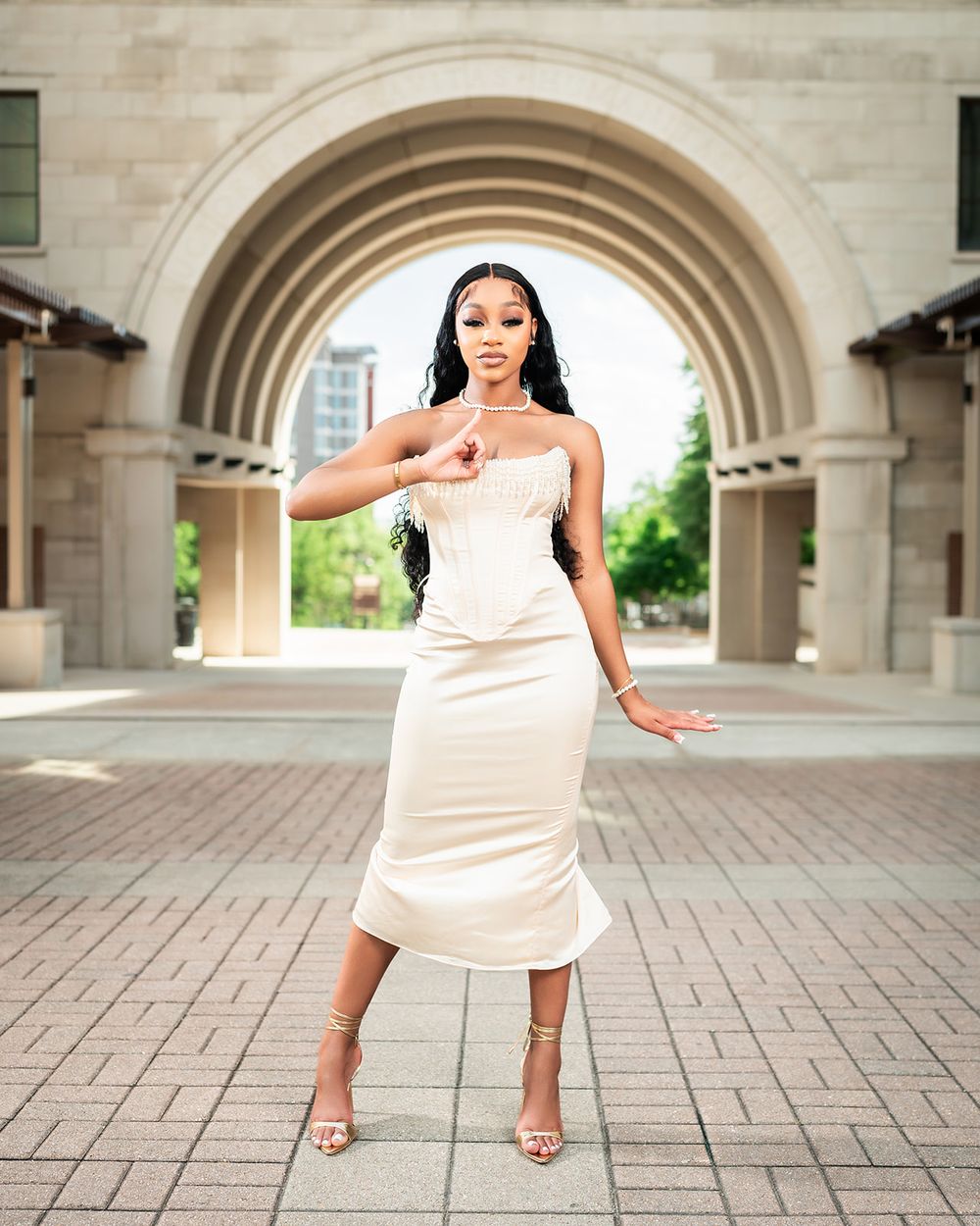 Elegant poses under stone archway wearing cream-colored formal dress.