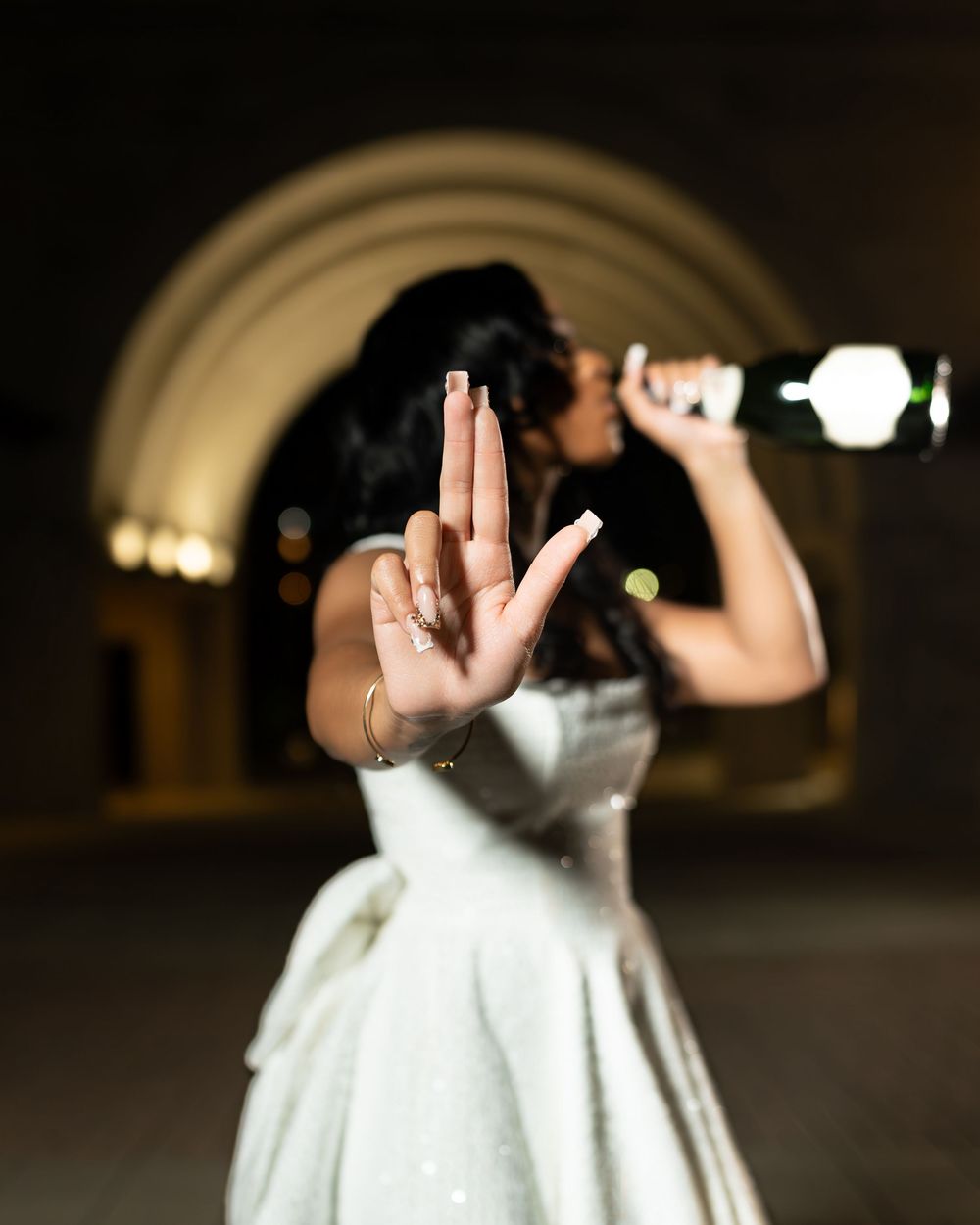 Graduate in white dress poses with creative hand gestures during evening photoshoot.