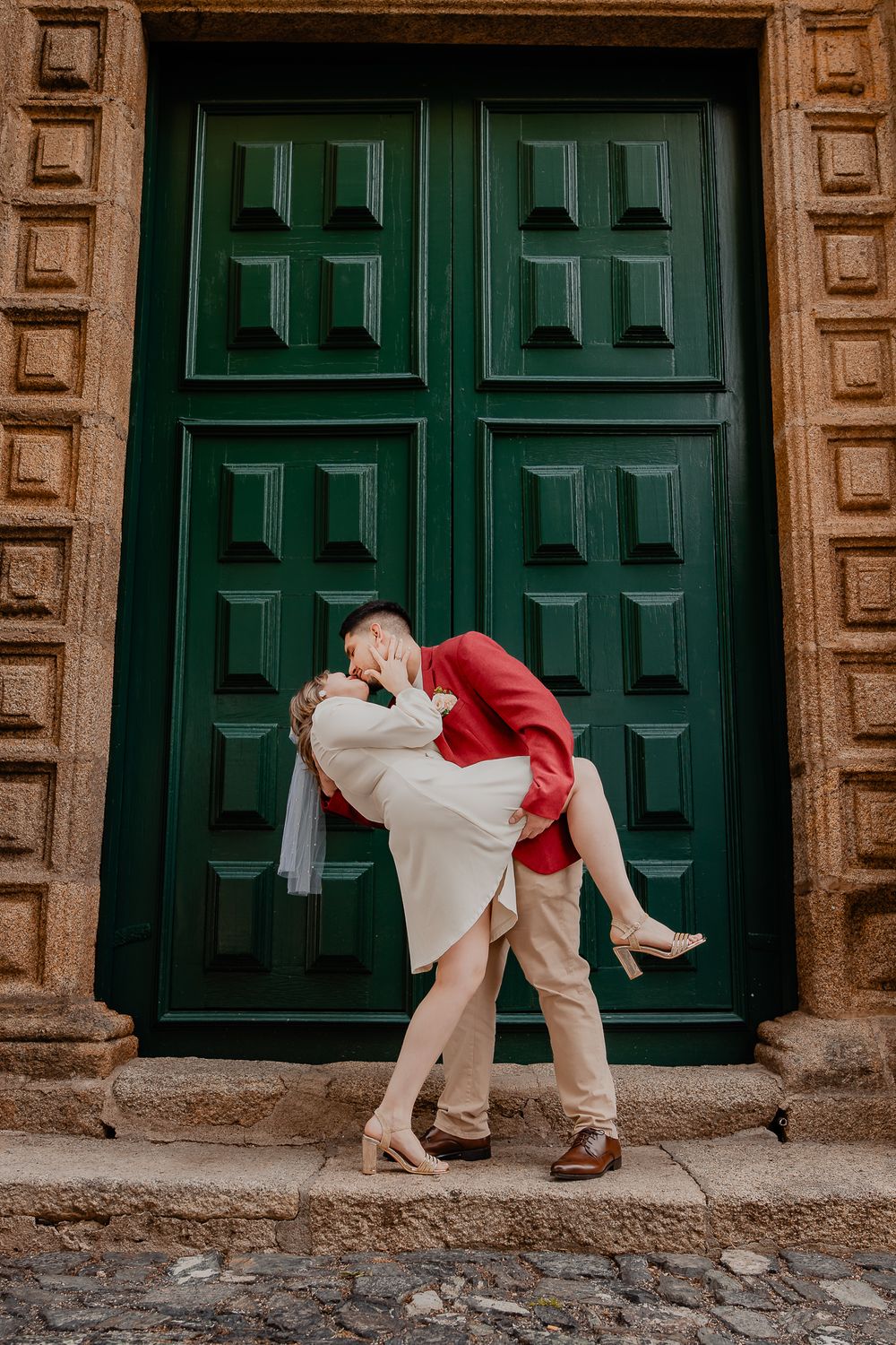 Playful couple poses in front of large green vintage doors.