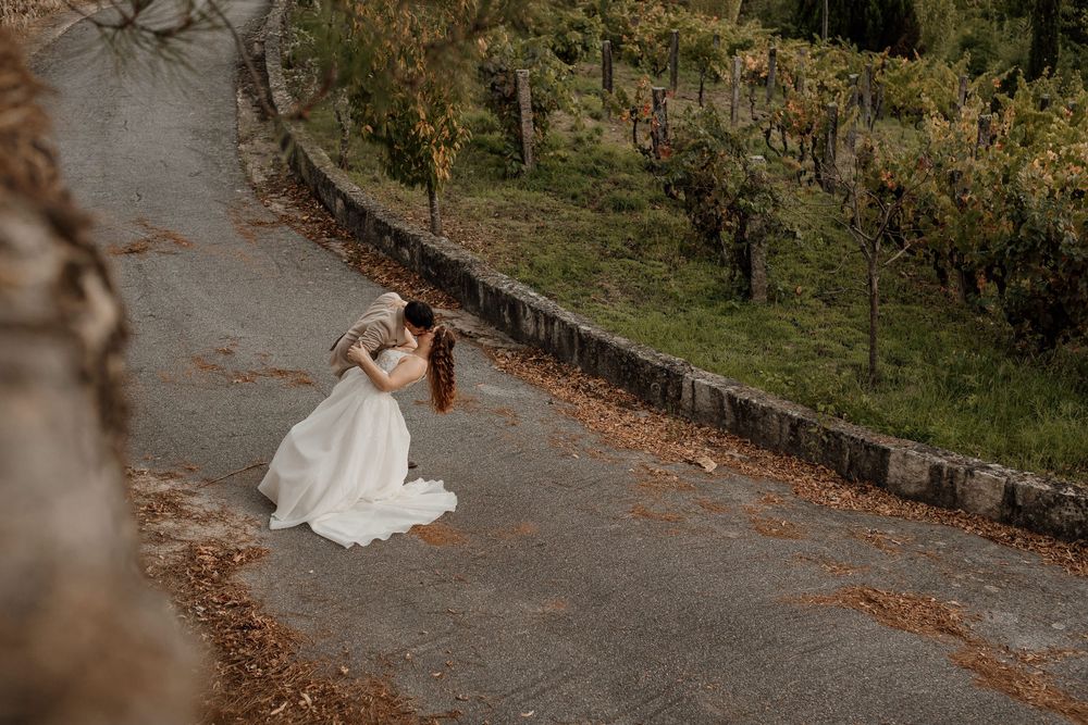 Bride and groom share a romantic embrace on a winding vineyard path surrounded by autumn foliage.