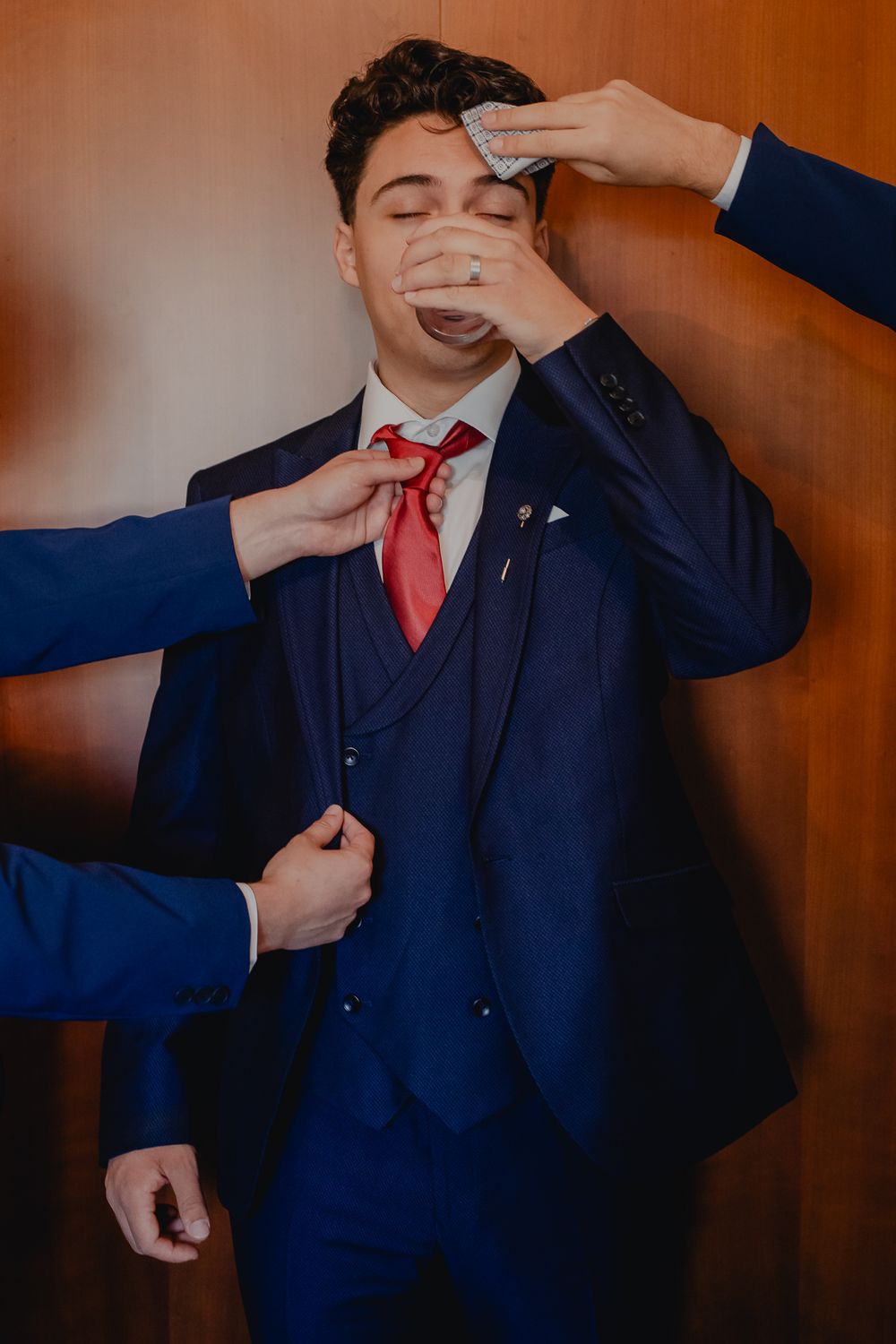 A groom in a navy suit being helped with final adjustments before the ceremony.