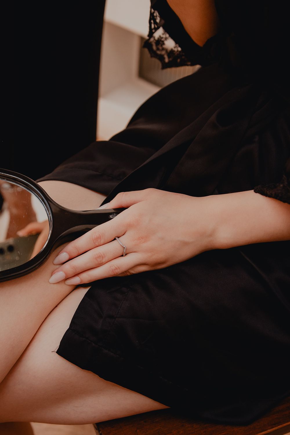 Close-up of a hand wearing an engagement ring resting on black fabric.