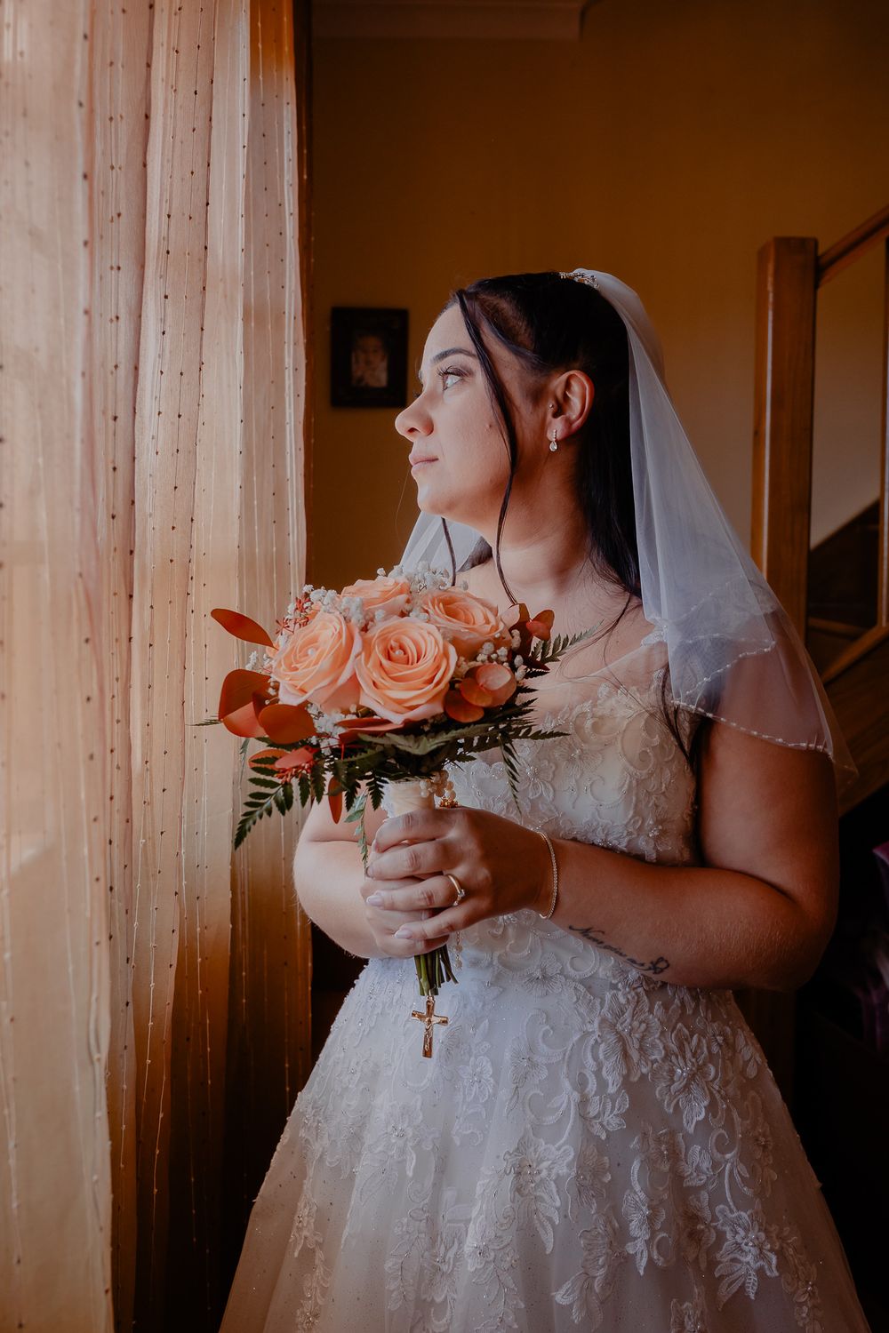Bride in white lace dress holding a bouquet near wooden pillars.