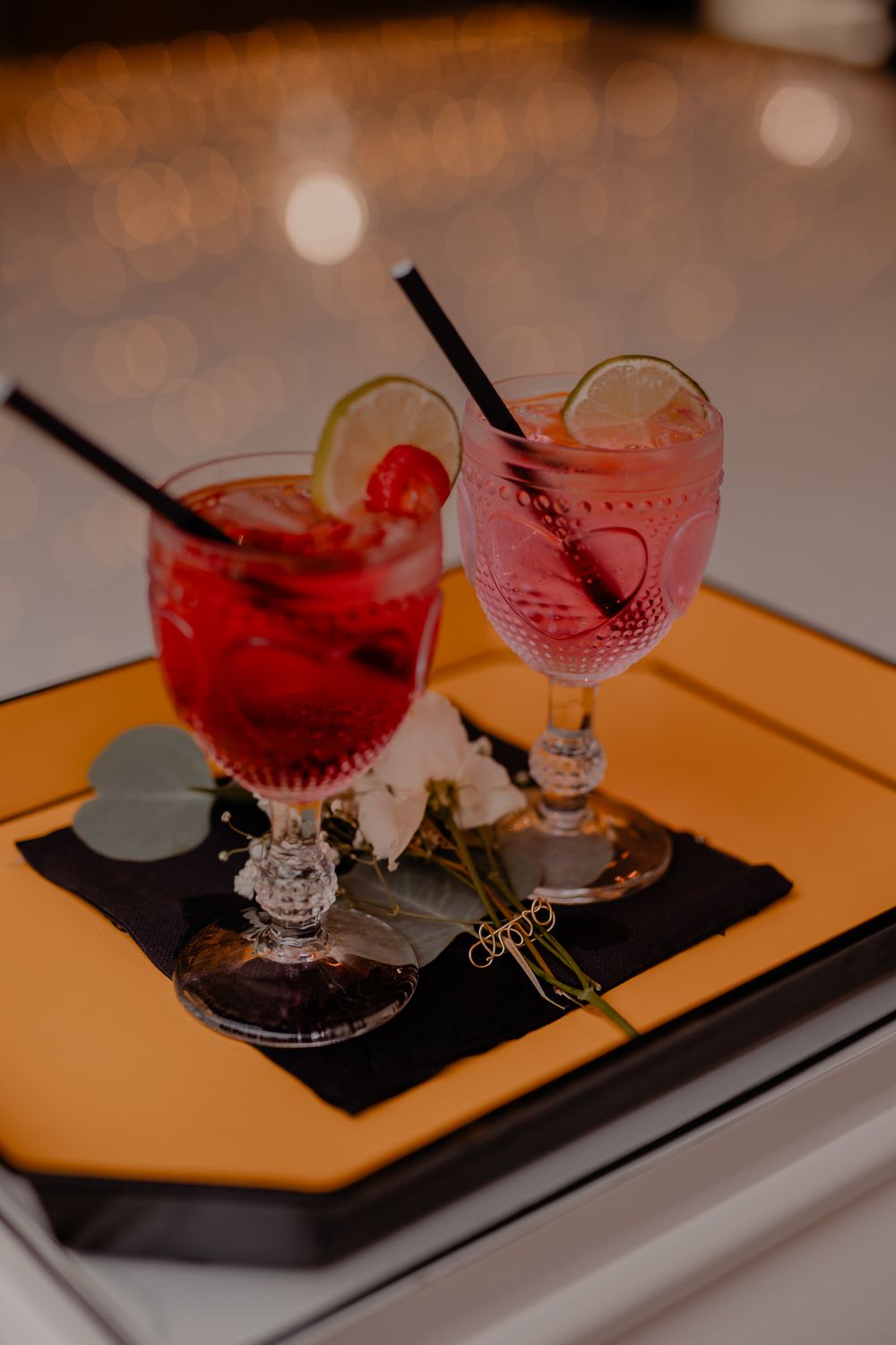 Pink cocktails with black straws served on modern geometric serving trays.