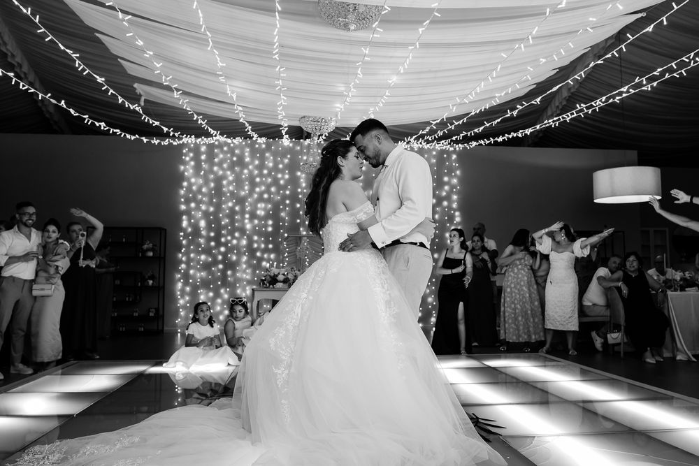Wedding reception dance floor illuminated with romantic string lights and white draping.