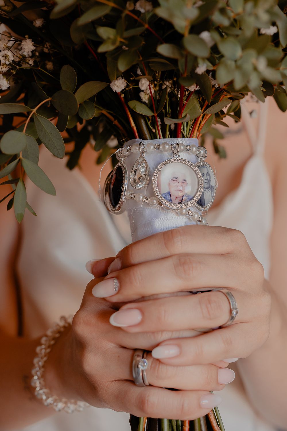 Close-up of hands holding a wedding bouquet adorned with vintage brooches and jewelry.