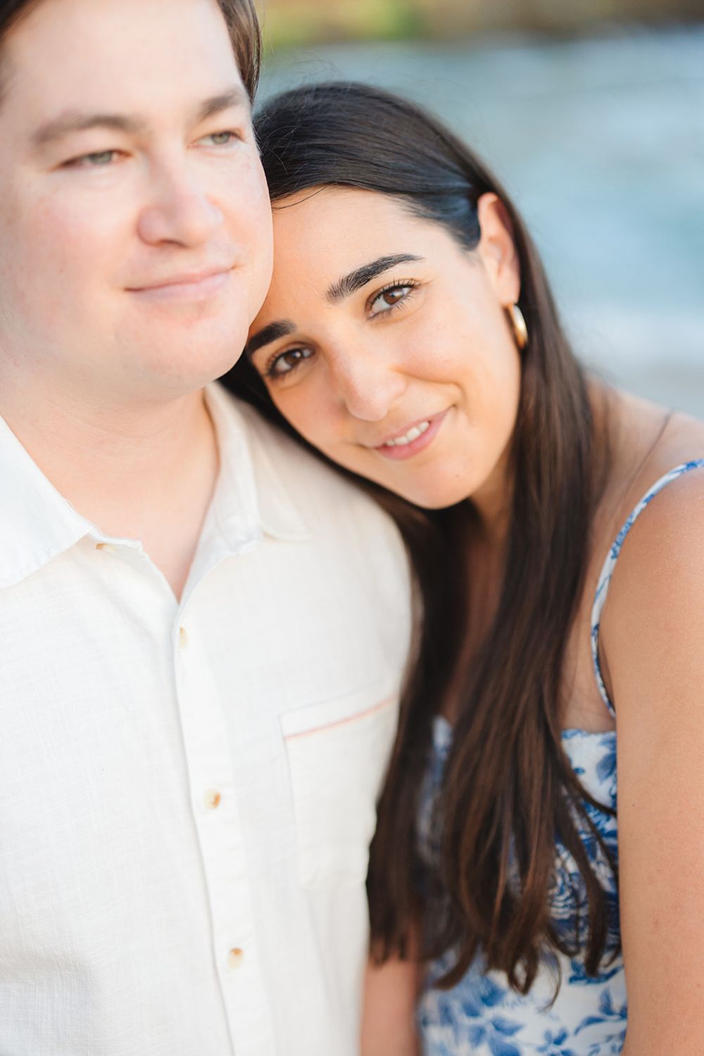 A close-up portrait of a couple smiling outdoors on a bright sunny day.