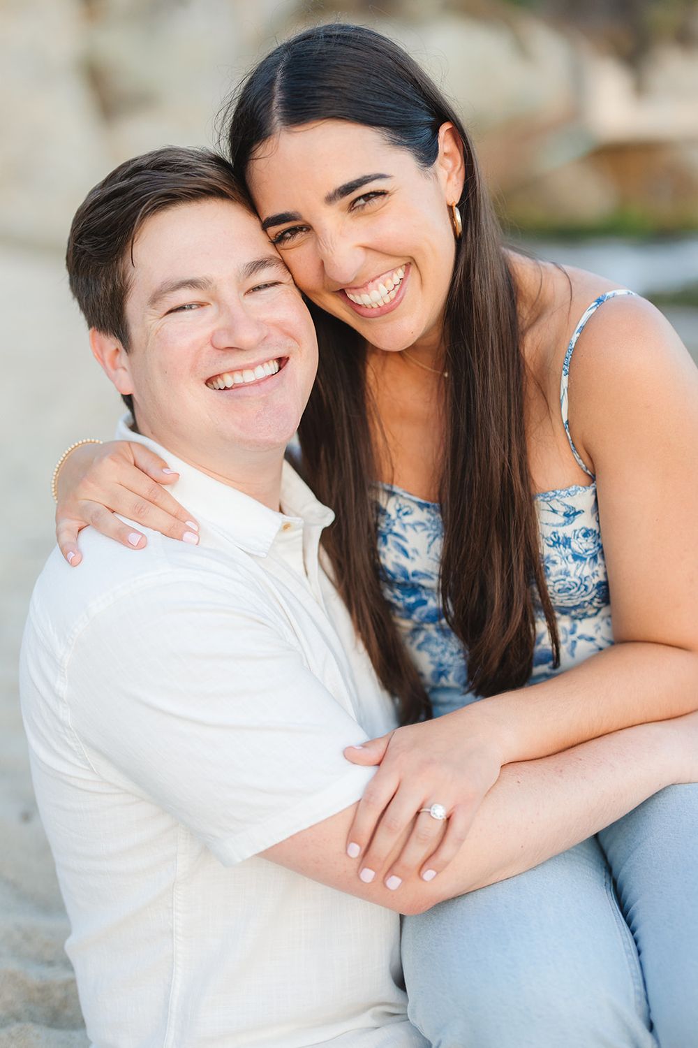 A couple smiling and embracing while sitting together outdoors in casual attire.
