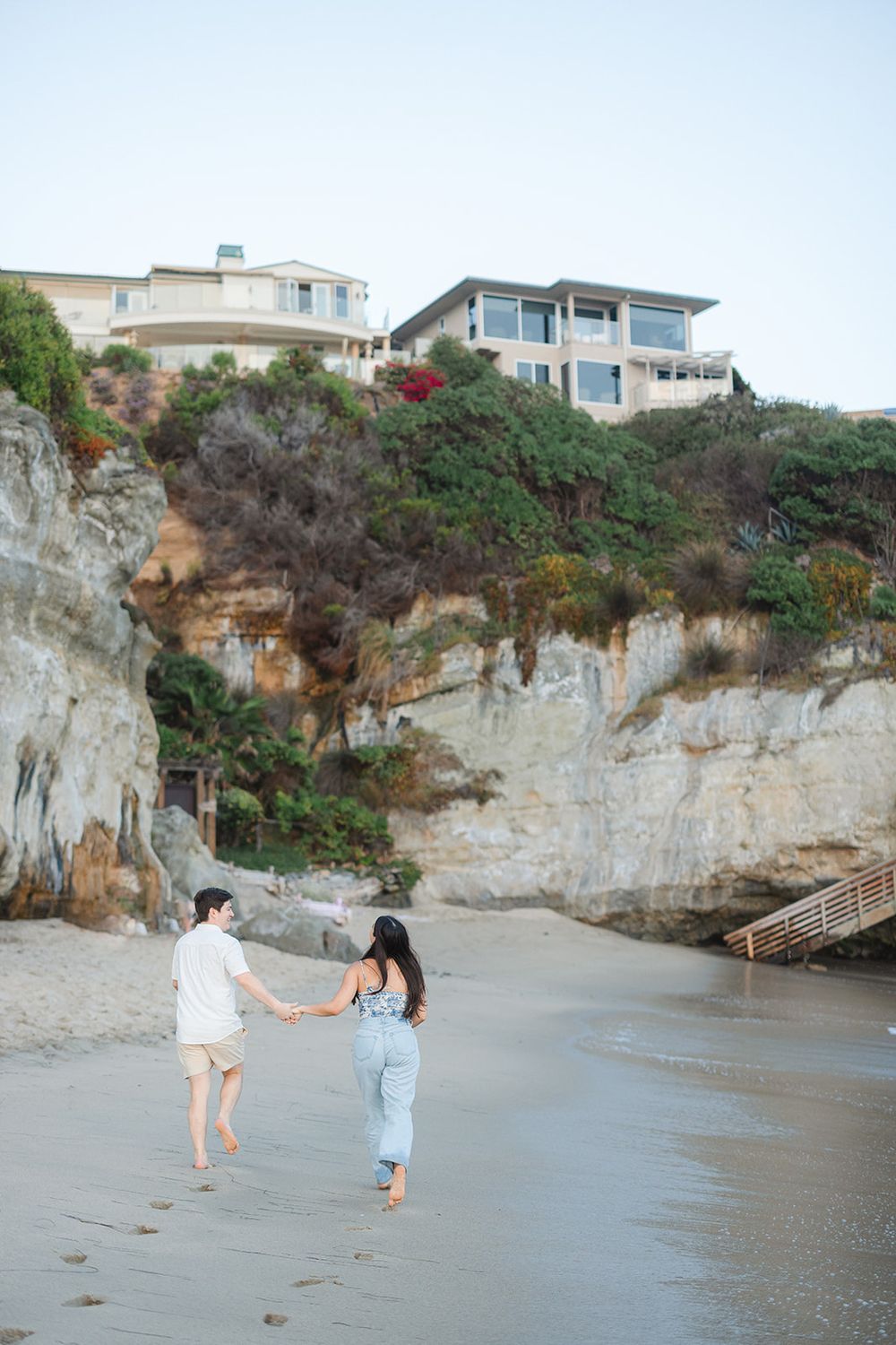 Two people stroll along a scenic beach with cliffs and coastal homes visible on the bluffs above.