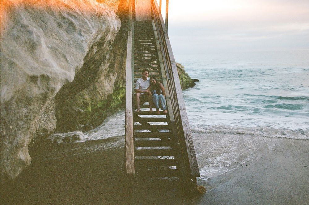 Rocky ocean staircase leads down to the beach with waves crashing against the cliffs at sunset.