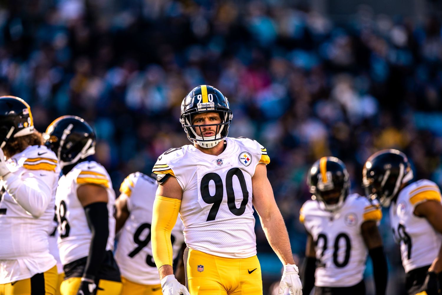 Pittsburgh Steelers #90 smiles on the field surrounded by teammates during an NFL game.