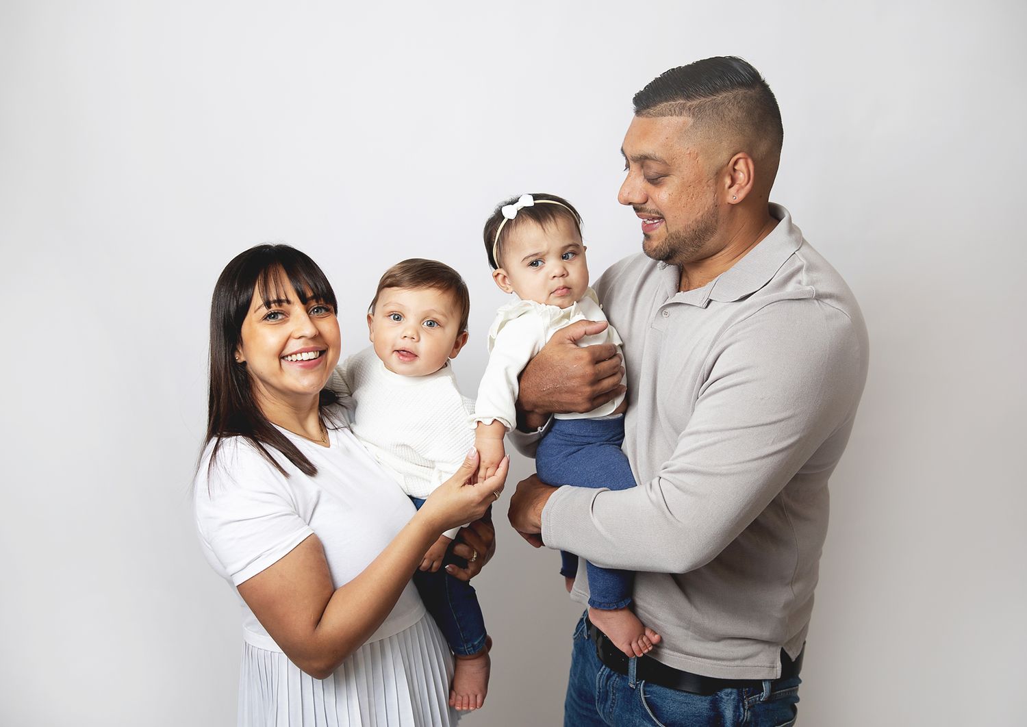A family of four poses together wearing white and grey casual clothing against a light background. During a family photoshoot in Bexley