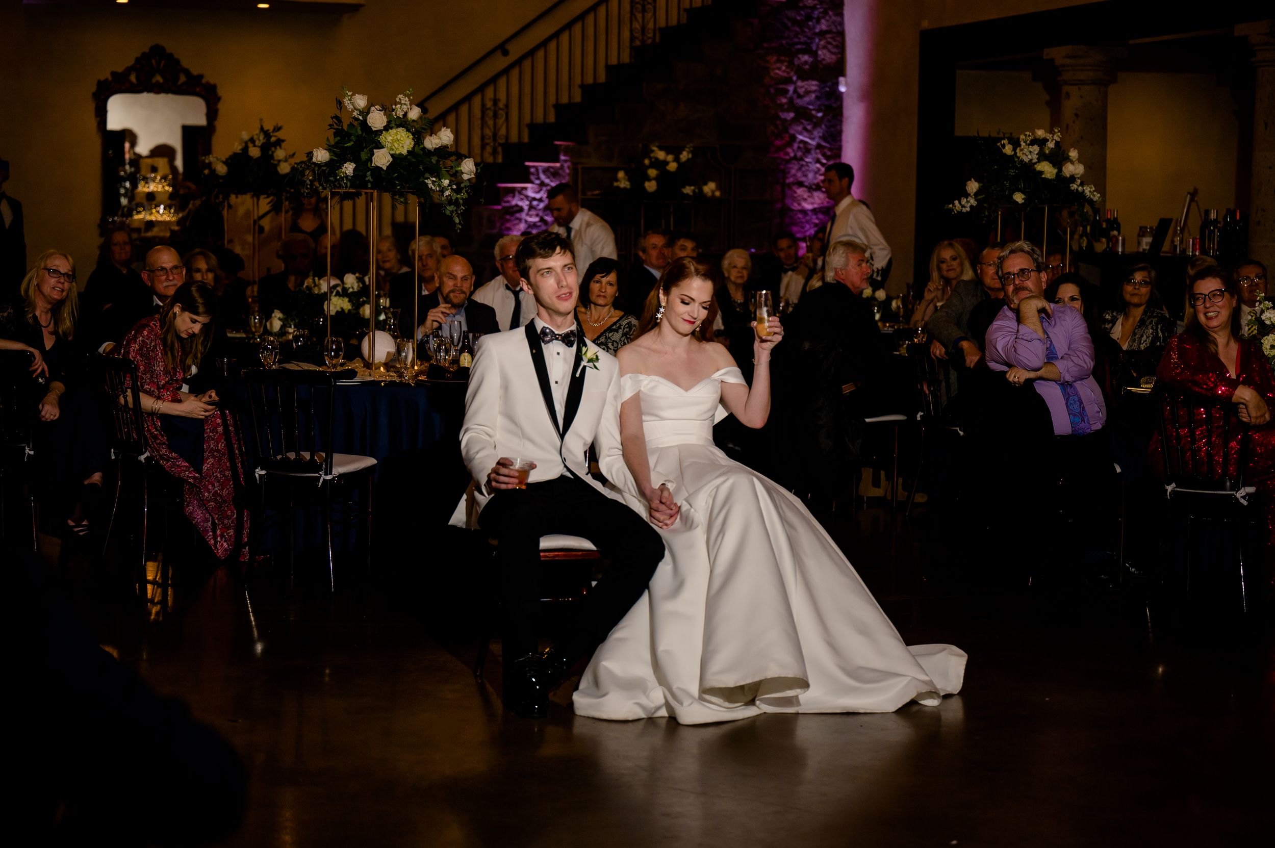 Wedding reception dance floor shows guests and wedding party celebrating in a dark ballroom setting.
