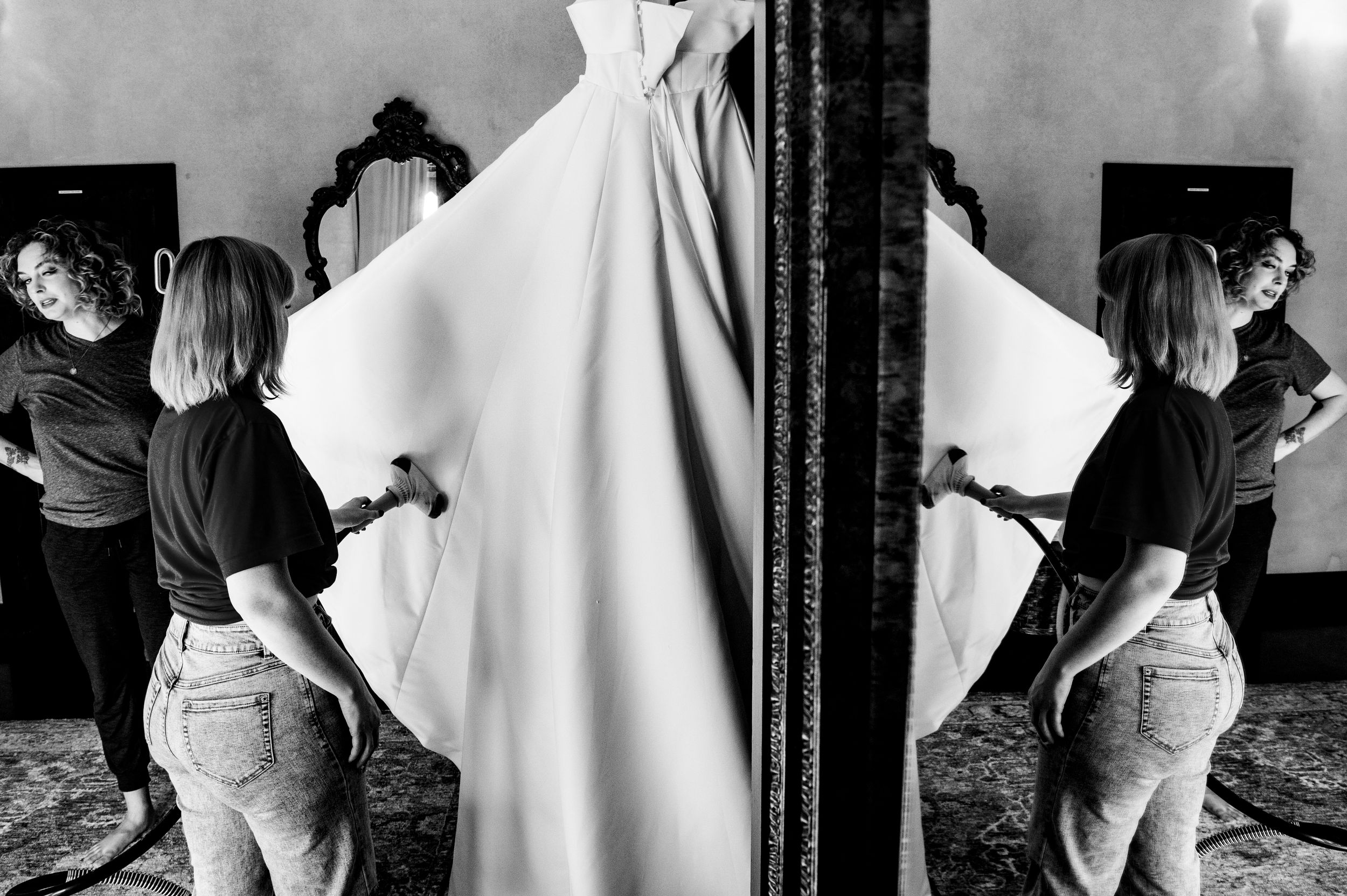 Black and white photo shows person hanging white fabric with a mirror creating symmetrical reflection effect.