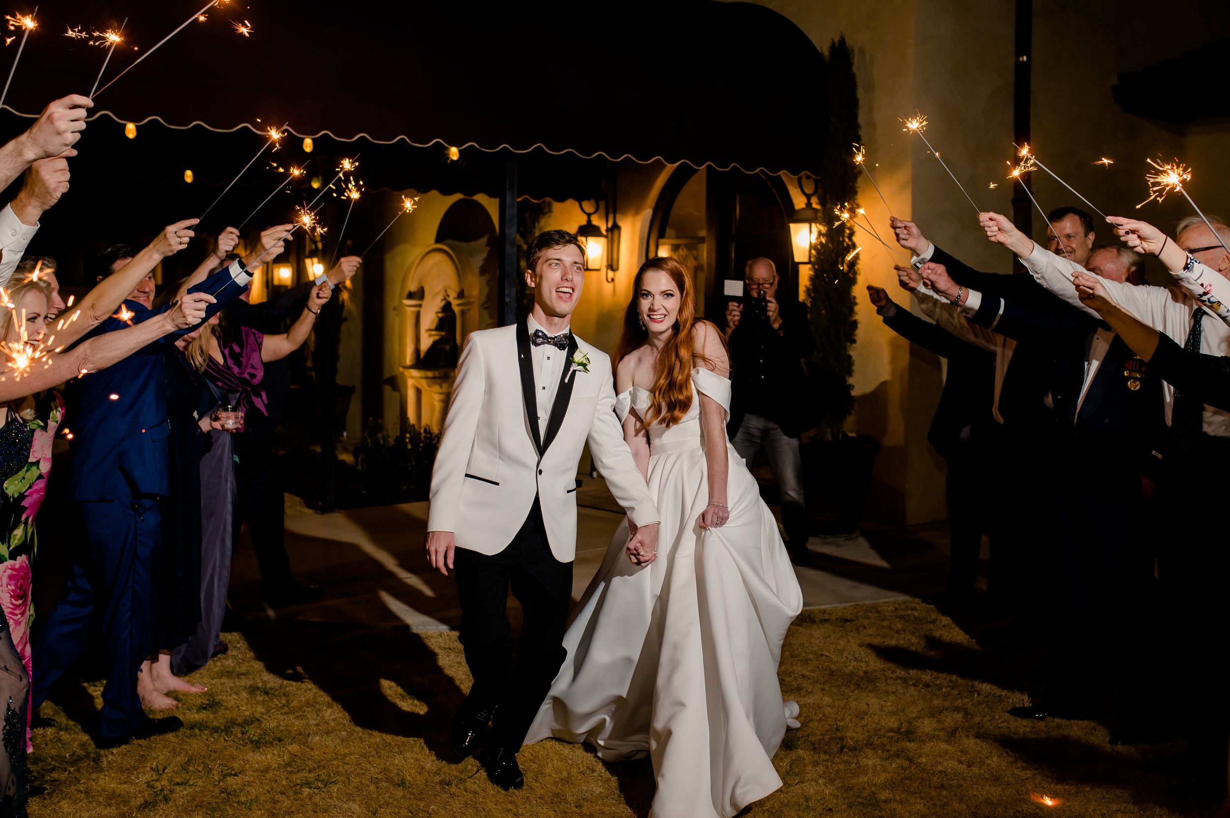 Newlyweds make their grand exit through a tunnel of sparklers held by wedding guests during an evening celebration.