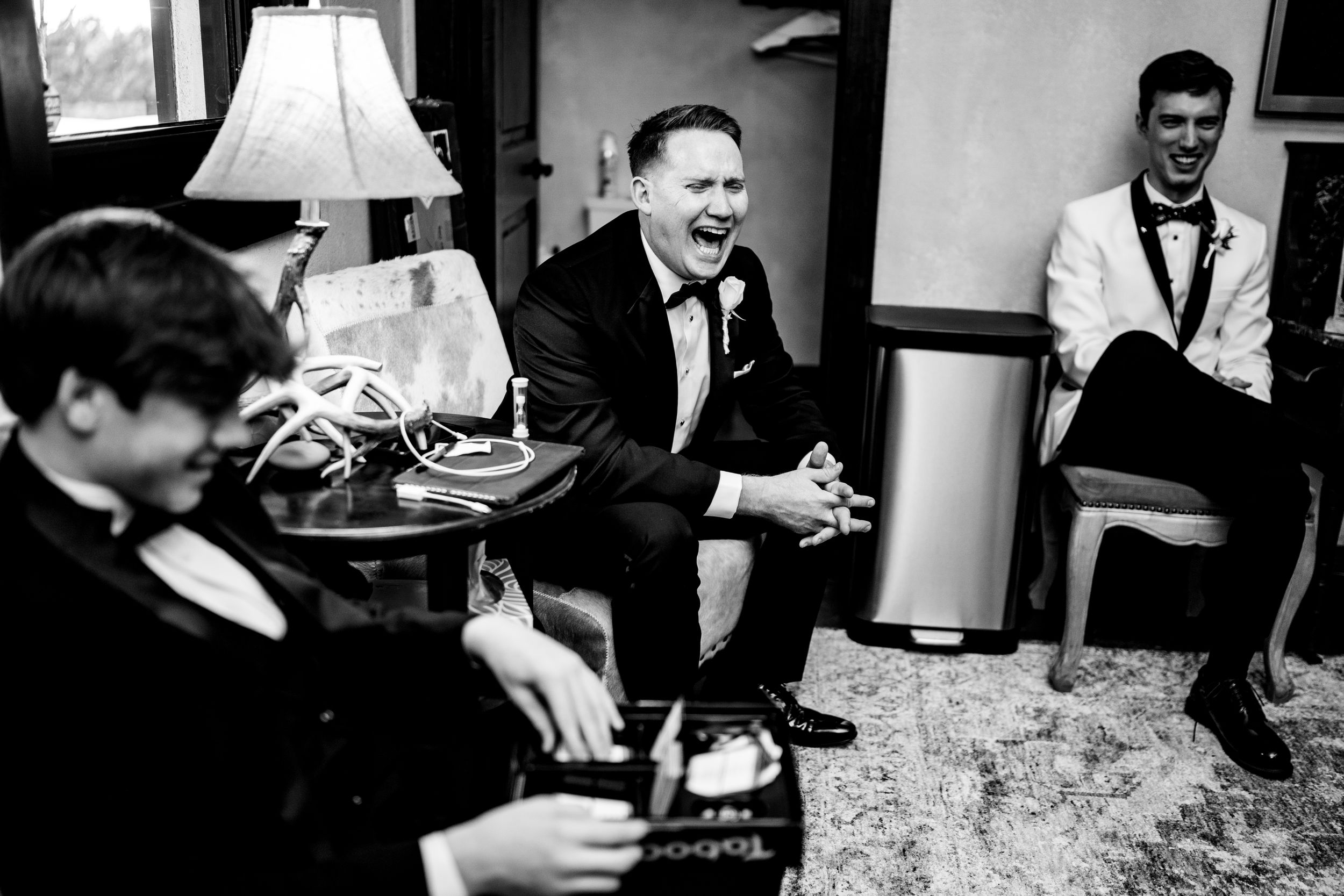 Black and white photograph of three people in formal attire gathered in a room around a lamp and sitting area.