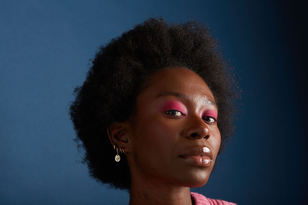 A portrait with bright pink eye makeup against a dark blue background.