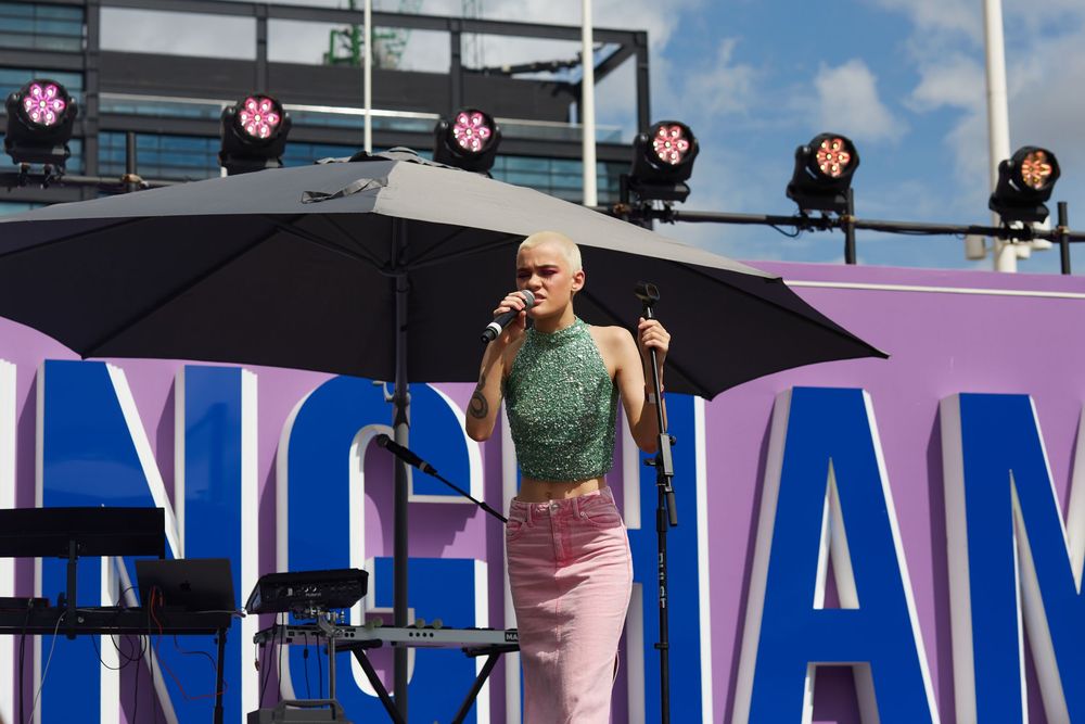 A performer on stage at an outdoor event with Birmingham signage and lighting equipment.